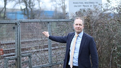 Richard Foord MP standing next to a railway holding the gate leading to the track