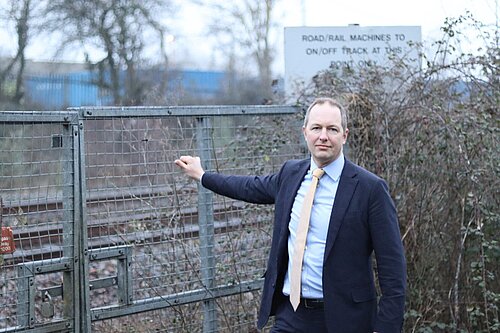 Richard Foord MP standing next to a railway holding the gate leading to the track