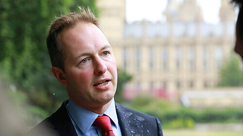 Richard Foord speaking to someone with the Houses of Parliament in the background