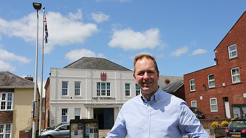 Richard Foord standing in front of Axminster Guildhall on a sunny day