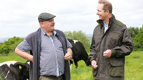Richard Foord walking and talking with a farmer in a cow field