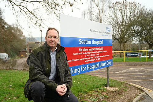 Richard Foord sitting in front of the sign for Seaton Hospital