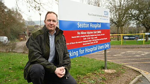 Richard Foord sitting in front of the sign for Seaton Hospital