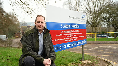 Richard Foord sitting in front of the sign for Seaton Hospital