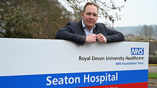 Richard Foord standing behind the sign for Seaton Hospital