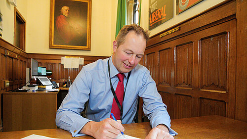 Richard Foord sitting at a desk and writing on a piece of paper